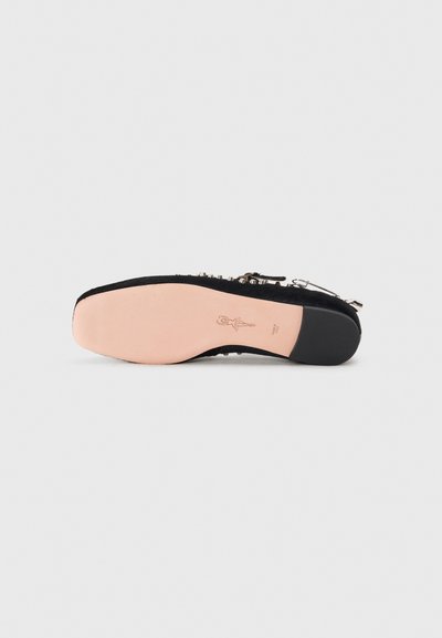 Chaussure plate noire avec une tige lisse, ornée de clous en argent décoratifs le long du bord et d'une semelle en caoutchouc rose clair avec une empreinte de logo.