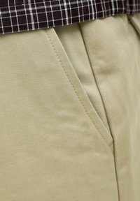 Poche de pantalon beige avec couture visible à côté d'un bas de chemise à carreaux marron et blanc.