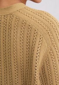 Strickjacke in einem gedämpften Gelbton mit einem strukturierten Muster aus vertikalen Linien, offener Arbeit und einem gerippten Kragen.