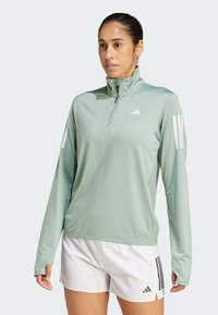 Limoengroene lange mouwen sporttop met een kwart-rits, voorzien van witte adidas strepen op de schouders en een zachte, lichte stof.