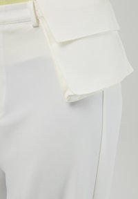 Pantalones blancos ajustados con un acabado de tela suave, bolsillo lateral con detalle de solapa y una silueta esculpida y ajustada.