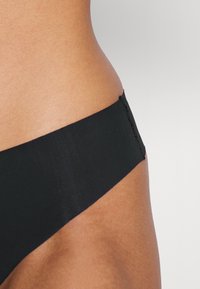 Czarne bikini dolne z gładkiego, elastycznego materiału, z czystym wykończeniem w pasie i minimalnym detalem szwów.