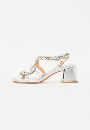 Sølv hælhe sandals med blokhæle og dekorative rhinestones. Har tynde remme og et åbent tådesign. Flad sål.