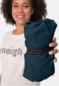 Insolito pacchetto di tessuto compatto di colore blu navy tenuto in mano, con una fascia nera che riporta la scritta "Realizzato con materiali riciclati". Texture liscia, design leggero.