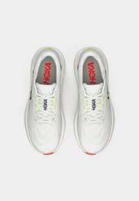 Ζευγάρι λευκά παπούτσια HOKA για τρέξιμο με επάνω μέρος από δίχτυ, κορδόνια και κόκκινο λογότυπο στην εσωτερική σόλα, απεικονισμένα από πάνω σε λευκό φόντο.