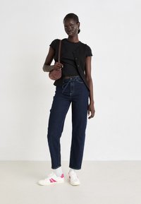 Black sleeveless vest over a black short-sleeve top, paired with high-waisted dark blue jeans and white sneakers with pink accents.