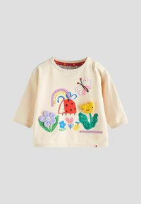 Cămașă din bumbac cu mâneci lungi de culoare crem deschis, cu design-uri colorate aplicate reprezentând un buburuză, un curcubeu, flori și o flutură.