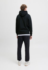 Zwarte hoodie met een trekkoordkap, gecombineerd met zwarte joggingbroeken. Beide items hebben een zachte textuur. Casual witte sneakers worden gedragen.