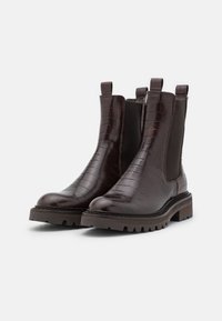 Bottines à motif crocodile marron avec des panneaux latéraux élastiques, des languettes de tirage et des semelles en caoutchouc épaisses. Talon épais pour une durabilité accrue.