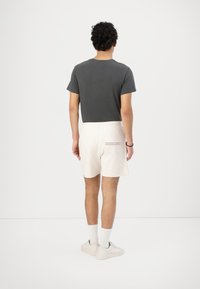 T-shirt grigio in cotone, pantaloni corti crema con un motivo testurizzato, calzini bianchi e sneaker chiare. Vista da dietro.