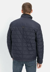 Mørkeblå quiltet jakke med høj krave, diamantmønster og letvægtsstof. Har et lille logo på den øverste del af ryggen.