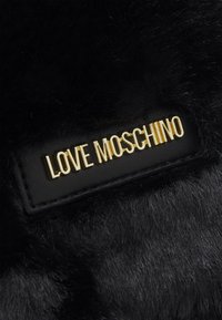 Černý materiál z umělé kožešiny s texturovaným povrchem, na kterém je zlaté logo "LOVE MOSCHINO" na černé kožené nášivce.
