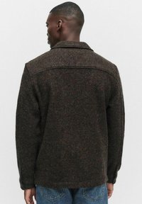 Brązowa kurtka z mieszanki wełny z wyrazistym kołnierzem, fakturowanym wykończeniem i luźnym krojem, noszona na niebieskich dżinsach.