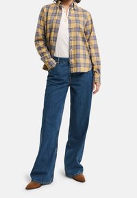 Gul og blå ternet skjorte med knapkrave, parret med højttaljede, brede blå jeans og brune spidse sko.