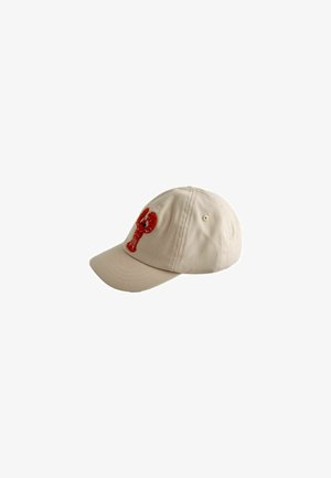 Gorra de béisbol beige con un cangrejo rojo bordado en la parte frontal, mostrada en ángulo para destacar el lado izquierdo y la visera curva.