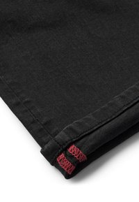 Țesătură de denim neagră cu o margine îndoioasă, având detalii de cusătură roșie. Textura este netedă, cu un ușor luciu.
