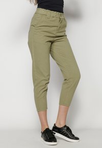 Pantalones cropped en color caqui con cinturilla elástica, bolsillos laterales y una textura suave; combinados con zapatillas negras con detalles de tachuelas.