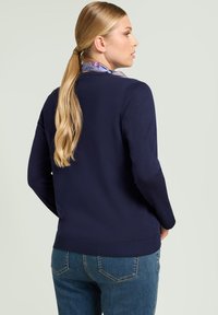 Maglione blu navy con maniche lunghe, scollatura rotonda e orlo a coste. Abbinato a jeans azzurri. Include una sciarpa multicolore intorno al collo.