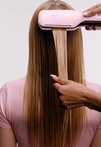 GHD Duet Style narzędzie do stylizacji w kolorze różowym, prostujące długie, gładkie, proste włosy z gładkim wykończeniem. Ręka trzyma sekcję włosów przy urządzeniu.