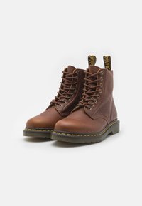 Bottines en cuir marron avec des orteils ronds, un design à lacets, des coutures jaunes et des côtés texturés ; avec une languette noire au niveau du talon.