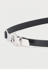 Μαύρη δερμάτινη ζώνη με ασημένια στρογγυλή αγκράφα και λαμπερό μεταλλικό κούμπωμα σε λευκό φόντο.