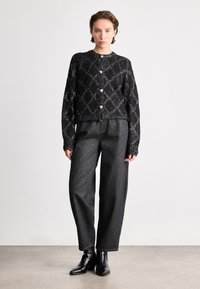 Cardigã preto em malha com um padrão de diamante e fio prateado, com botões redondos. Combinado com calças de ganga escuras de cintura alta e botas de tornozelo.