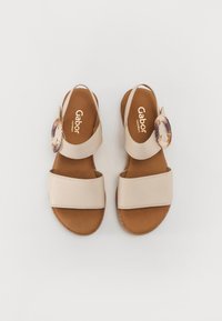 Beige leather sandals with two wide straps, brown insoles, and an accent ring detail on the side. Smooth texture and flat soles.