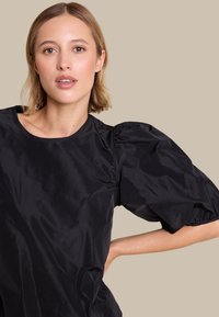 Svart topp med pufferm i glatt, skinnende stoff med rund hals, som har rynkede detaljer på ermene og en avslappet passform.