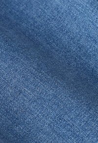 Tissu en denim bleu clair avec une texture lisse et un motif de tissage visible, présentant de légères usures et des variations de couleur.