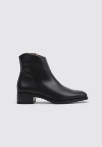 Botín de cuero negro con un diseño elegante, puntera redondeada, tacón bajo y detalle de costura minimalista en el lateral.