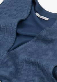 Prenda de color azul marino con un patrón de espiga texturizado. Tela suave, cuello redondeado y una etiqueta que dice "DAN JOHN" en el interior.