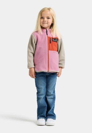 Fleecejacke mit rosa Körper, grauen Ärmeln und orangefarbener Brusttasche. Kombiniert mit blauen Jeans und weißen Turnschuhen. Leichtes Material, Reißverschluss.