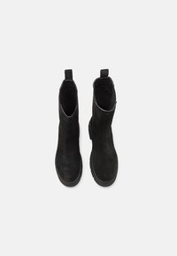 Paire de bottines en daim noir avec bouts ronds, languettes à l'arrière et semelles épaisses en caoutchouc, vues de dessus sur un fond clair.