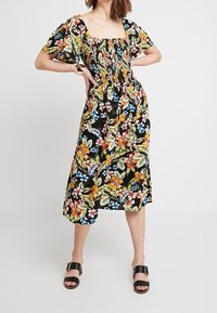 Czarna sukienka w kwiaty z kwadratowym dekoltem, krótkimi bufiastymi rękawami i marszczonym stanikem. Posiada kolorowe kwiaty i liście w żywych odcieniach.
