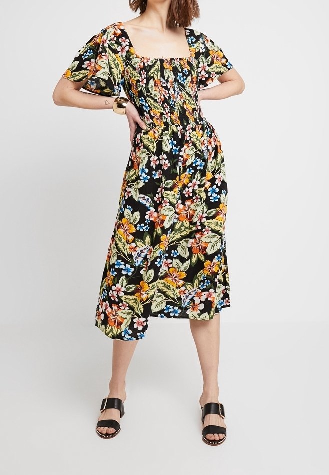 Czarna sukienka w kwiaty z kwadratowym dekoltem, krótkimi bufiastymi rękawami i marszczonym stanikem. Posiada kolorowe kwiaty i liście w żywych odcieniach.