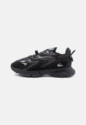 Black athletic shoes with a mesh upper, suede accents, and textured midsole. Features reflective details and green laces.