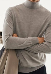 Grauer Rollkragenpullover aus weichem Strickmaterial, mit langen Ärmeln und gerippte Bündchen, kombiniert mit einer hellen Außenjacke.