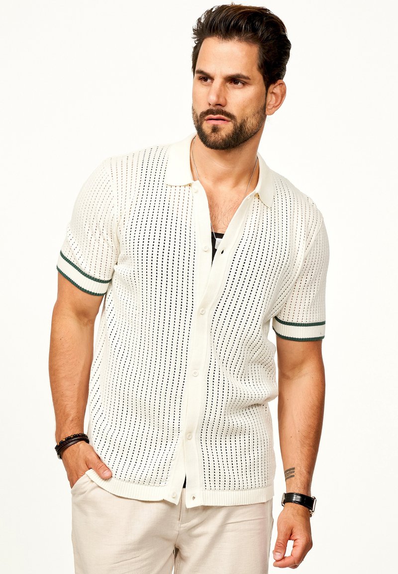 Kurzarm, gestricktes Hemd in Creme mit offenen Mustern, grün gestreiften Bündchen und Knopfverschluss, das eine strukturierte Oberfläche aufweist.