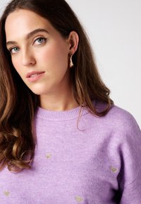 Lavender trui met een ronde halslijn, voorzien van kleine gouden hartpatronen. De stof lijkt zacht en gestructureerd.