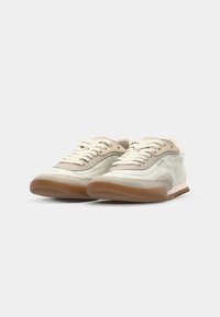 Sneakers bianchi in tela con accenti beige, suola in gomma e dettagli testurizzati. Presentano lacci piatti e un design a bassa altezza.