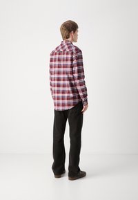 Camicia a maniche lunghe con motivo a quadri rosso, blu e bianco, caratterizzata da un colletto con bottoni e un orlo arrotondato, abbinata a pantaloni neri.