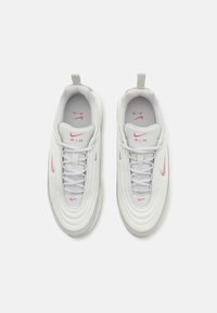 Weiße Sportschuhe mit pinkem Nike-Logo, strukturiertem Obermaterial, runder Form, Schnürverschluss und einer Lasche an der Rückseite für einfaches Anziehen.