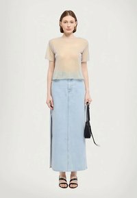 Top beige trasparente a maniche corte abbinato a una gonna midi in denim azzurra con spacchi laterali e sandali neri con cinturini. Borsa nera in mano.