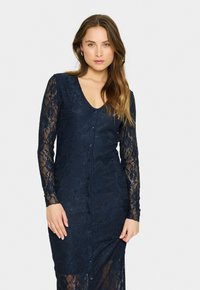 Navy lace dress with long sleeves, v-neck, and button closure. Features intricate floral patterns and a fitted silhouette, partially sheer at the bottom.