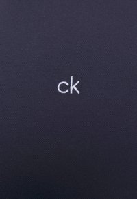 Navy fabric features discreet white "ck" logo, showcasing a textured surface with a modern, minimalistic design.
