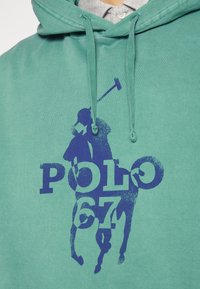 Türkisfarbener Hoodie aus Baumwolle mit einem großen dunkelblauen Grafikmotiv eines Polo-Spielers und dem Text "POLO 67". Verstellbare Kapuze mit Kordelzug.
