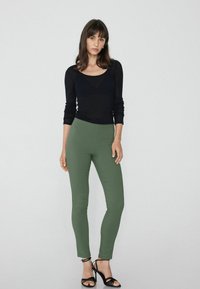 Černý top s dlouhým rukávem a kulatým výstřihem, kombinovaný s olivově zelenými přiléhavými legínami. Model má na sobě černé sandály na podpatku.