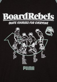 Fekete póló, fehér szöveggel: "BoardRebels" és "MINDENKI SZÁMÁRA SKATE TANFOLYAMOK". A pólón gördeszkázók illusztrációi, akik trükköket mutatnak be, lépésről lépésre utasításokkal.