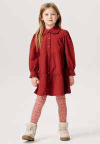 Röd knappröd klänning med volangkrage och puffärmar, kombinerad med mönstrade rosa leggings och beigea pälsstövlar.