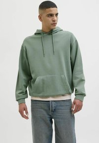 Lys grøn hættejakke med en frontlomme, snoretræk og ribbede manchetter, parret med blå jeans. Blød tekstur, afslappet design.